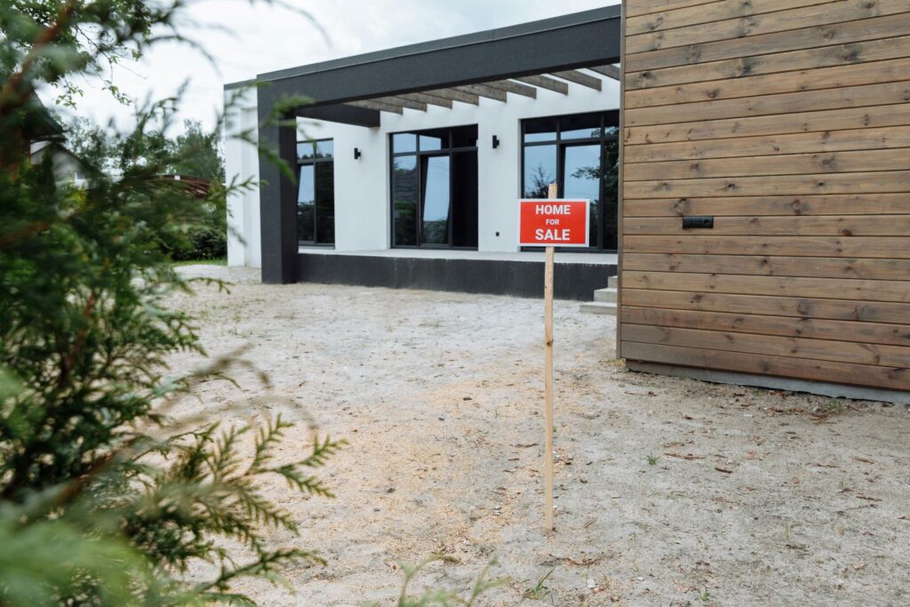 Small red for sale sign on the side of a modern home